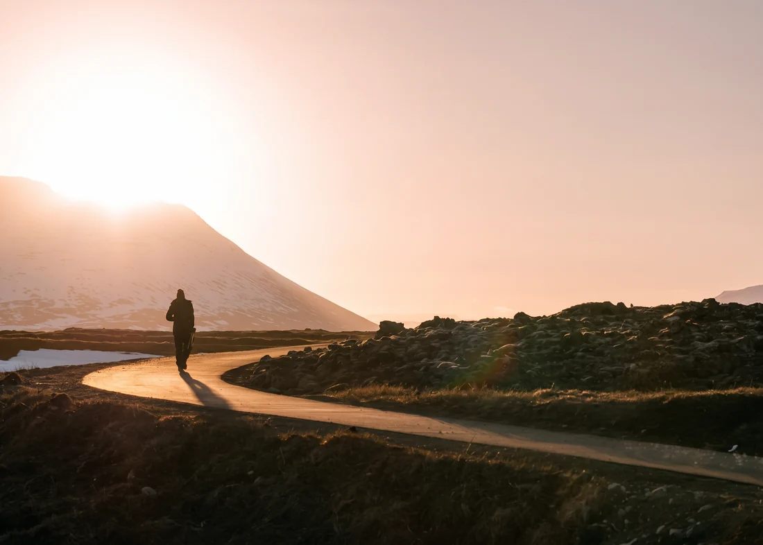 A person walking a winding path toward warm mountain sunlight